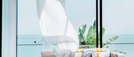 A modern living room with a large window overlooking the sea, featuring a sofa and a coffee table.