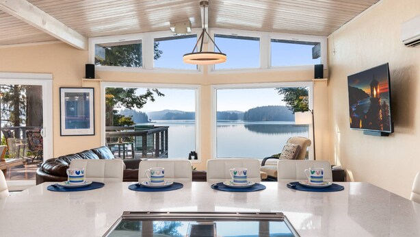 A modern kitchen with a large island, large windows with a lake view, and a dining area with chairs and a table.
