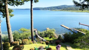 A lakeside view with a dock, a grassy area with a fire pit, and a clear view of the lake.