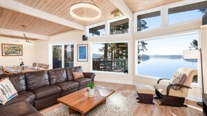 A spacious living room with a brown leather sofa, a wooden coffee table, and a view of a lake through large windows.