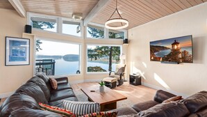 A spacious living room with a large leather sofa, a wooden coffee table, and a view of a lake through large windows.