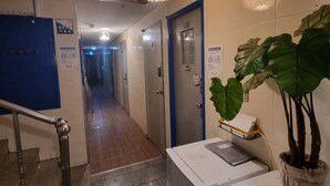 A hotel corridor with a blue door marked 101, a staircase with metal railings, a ceiling light fixture, and a potted plant. - kinghouse (Gwangju)