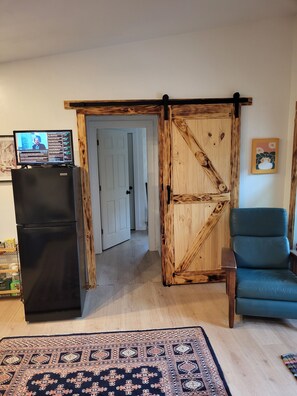 A kitchen with a black refrigerator, a wooden door, a blue chair, and a patterned rug. - Terry Hill Little Lodge, Cozy, Luxury Comfort overlooking beautiful Keuka Lake! (Hammondsport)