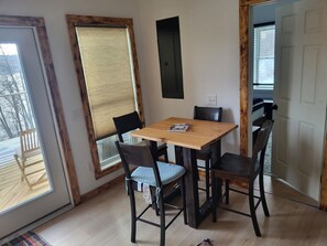 A dining area with a wooden table and four chairs, large windows with blinds, and a view of the outdoors. - Terry Hill Little Lodge, Cozy, Luxury Comfort overlooking beautiful Keuka Lake! (Hammondsport)