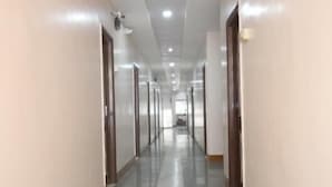 Un pasillo largo y estrecho con paredes blancas y suelo gris, que lleva a una habitación al final.