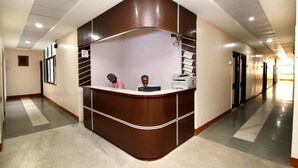 Mostrador de recepción con dos empleados, diseño curvo y un pasillo con puertas y ventanas.