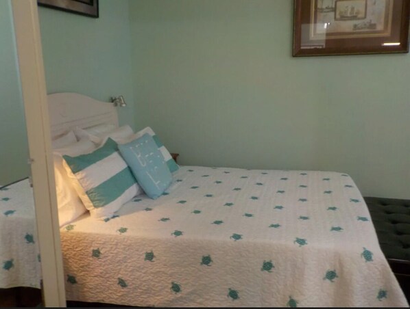 A bed with a white quilt and green leaf patterns, a blue pillow, and a white headboard. - Charming cottage in Pensacola (Pensacola)