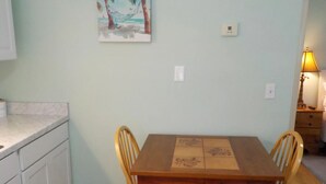 Un comedor con una mesa y sillas de madera, una pared de color claro y un cuadro de una playa.
