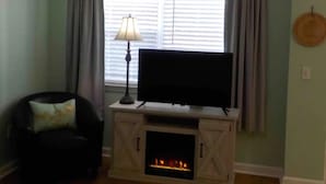 Una sala de estar con chimenea, un televisor sobre un mueble bajo, una silla y una lámpara.
