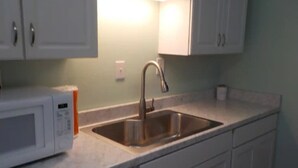 Una cocina con un lavamanos de acero inoxidable, un microondas blanco y armarios blancos.