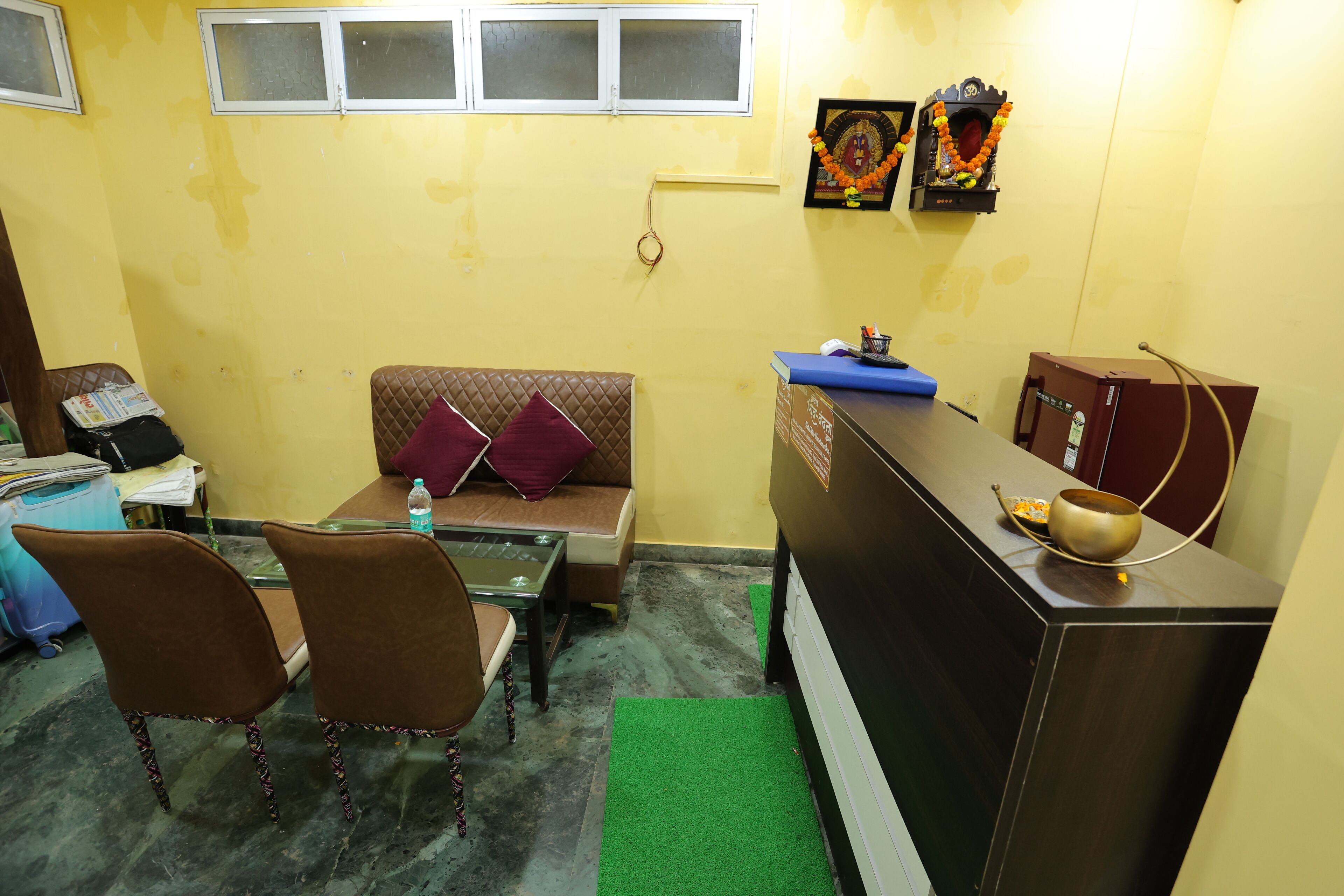 A compact room with a sofa, two chairs, a small table, a water bottle, a decorative item on the wall, and a small cabinet.