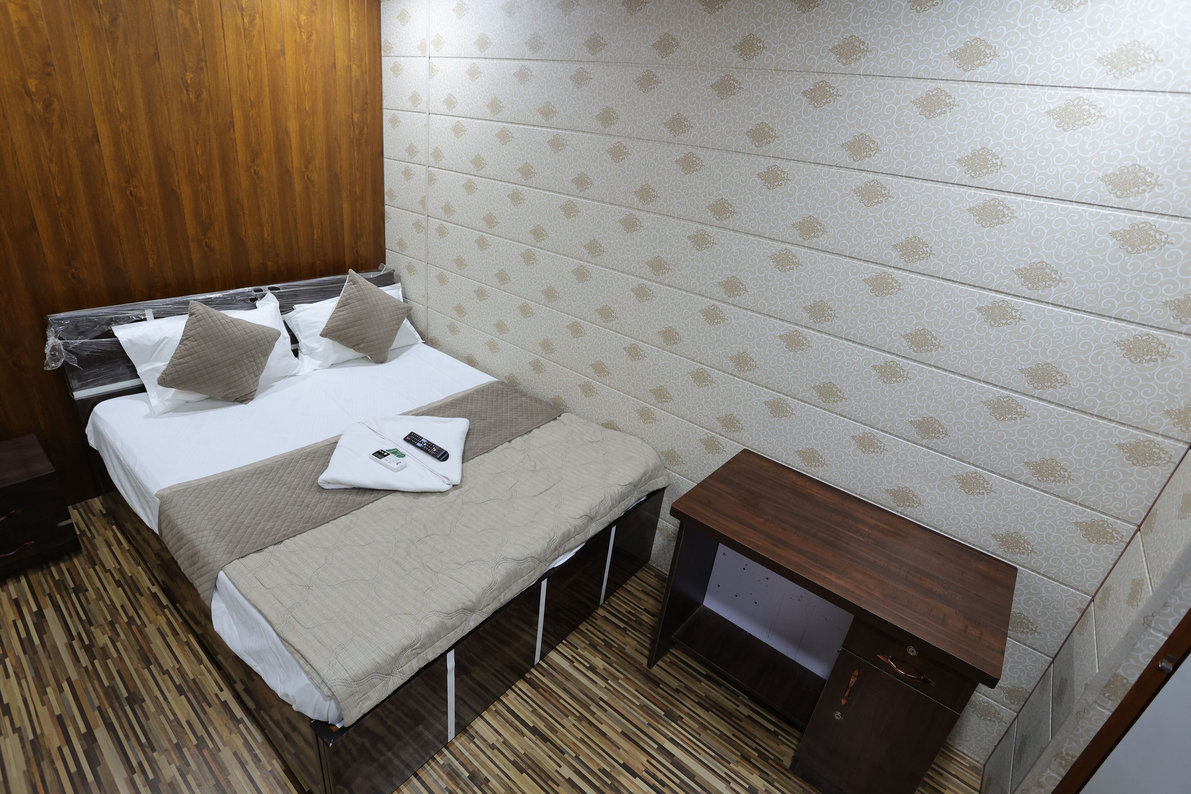 A hotel room with a bed, a bench, a wooden nightstand, and a patterned wall.