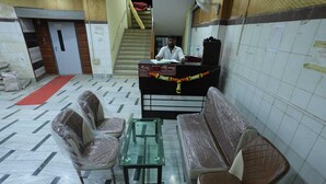 Zona de recepción con mostrador, dos sillones acolchados, una mesa de vidrio y una escalera al fondo.