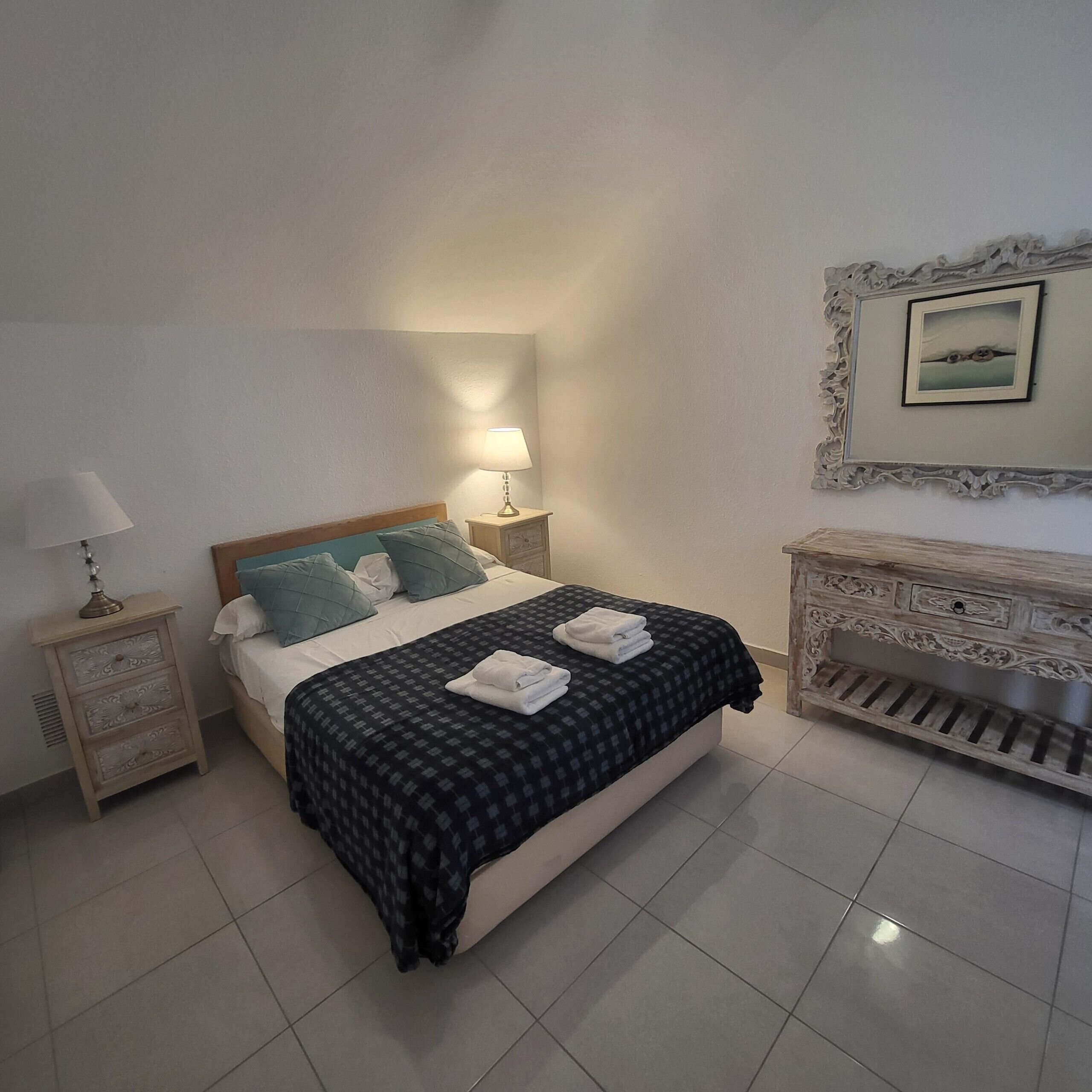 A neatly arranged bedroom with a bed, bedside lamps, a dresser, and a framed picture on the wall.