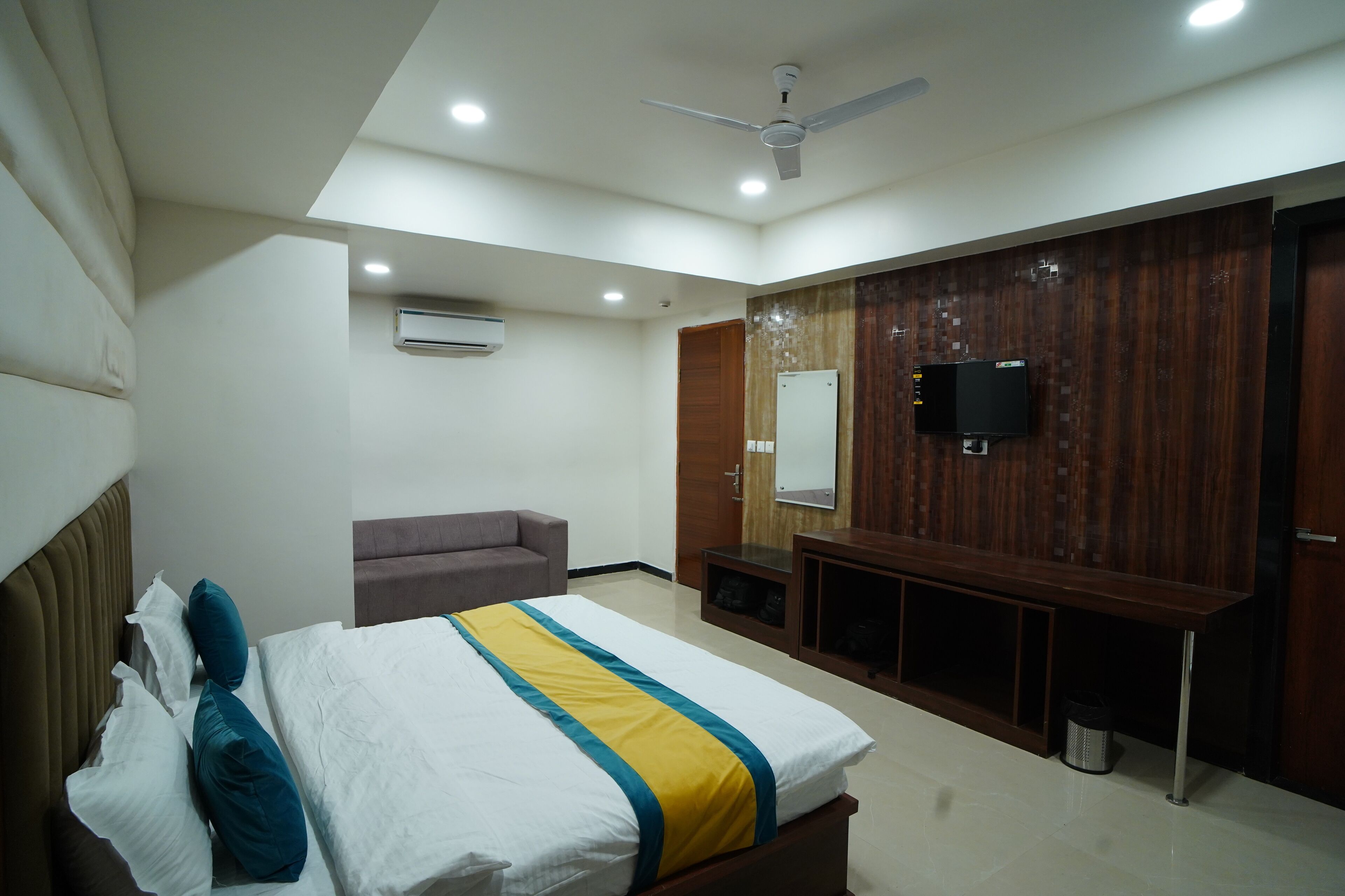 Una habitación de hotel moderna con cama, sofá, televisor y pared de paneles de madera.