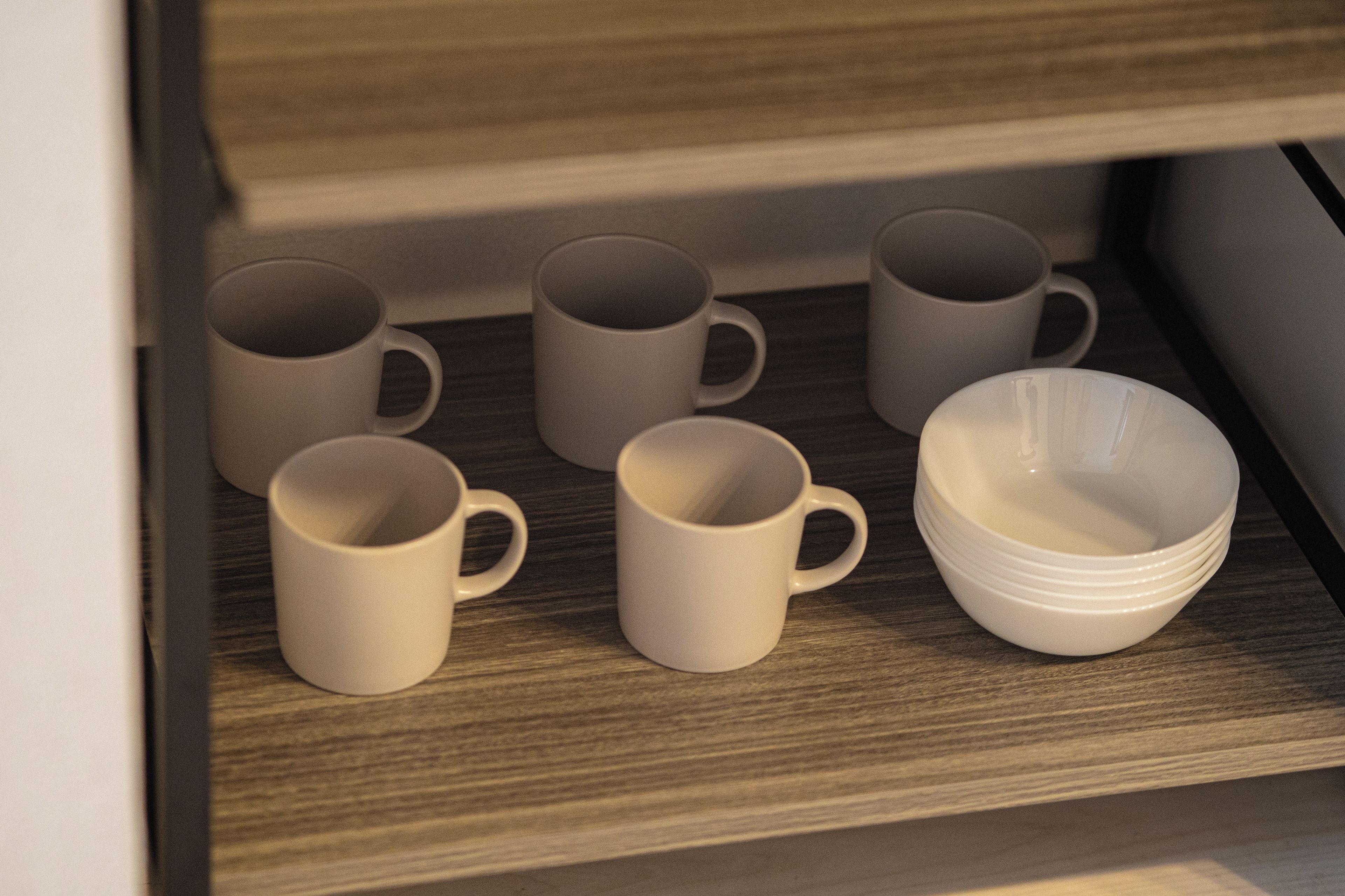 Een verzameling witte mokken en kommen op een houten plank.