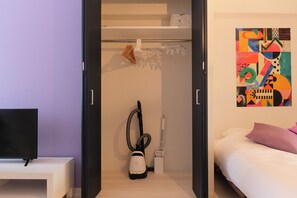 Una habitación moderna con una cama, un televisor, una aspiradora y un cuadro abstracto y colorido en la pared.