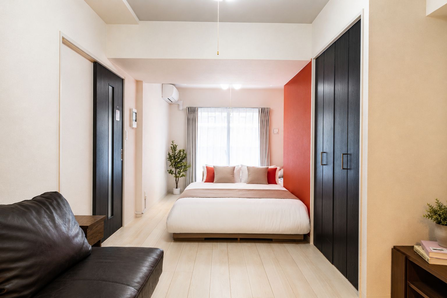 A modern bedroom with a bed, a dark-colored sofa, a wardrobe, and a potted plant.
