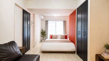 Quarto moderno com cama, sofá escuro, guarda-roupa e planta em vaso.