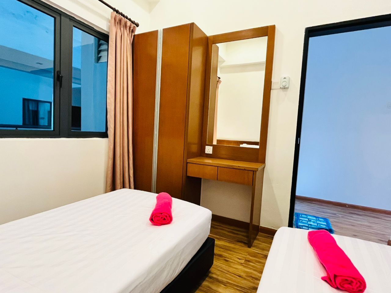 A hotel room with two beds, a wooden desk, a mirror, and a sliding door leading to a balcony.
