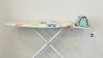 Una tabla de planchar con funda estampada y un planchador azul sobre una pared blanca.