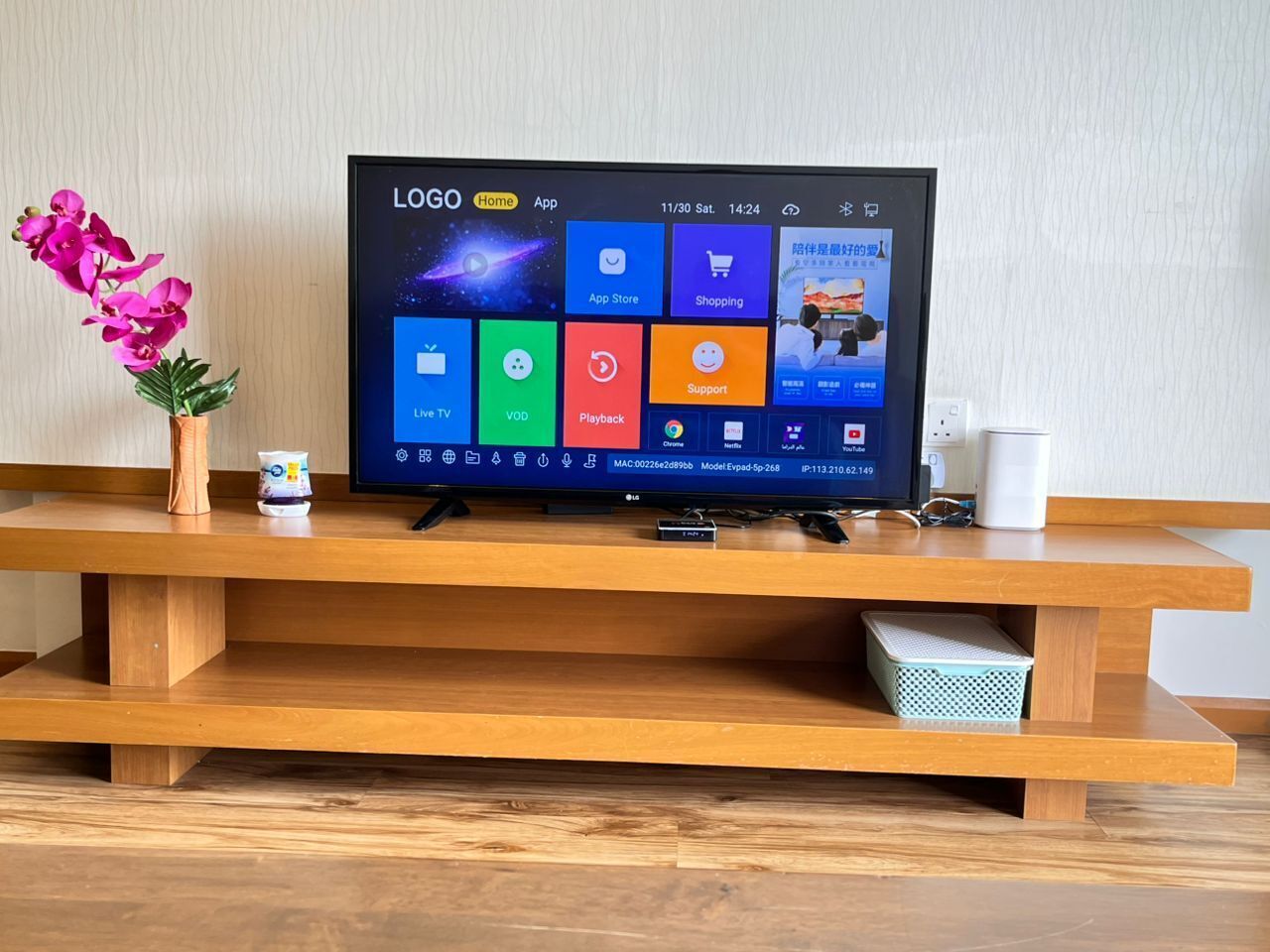 A television on a wooden stand with a flower vase and a cup beside it.