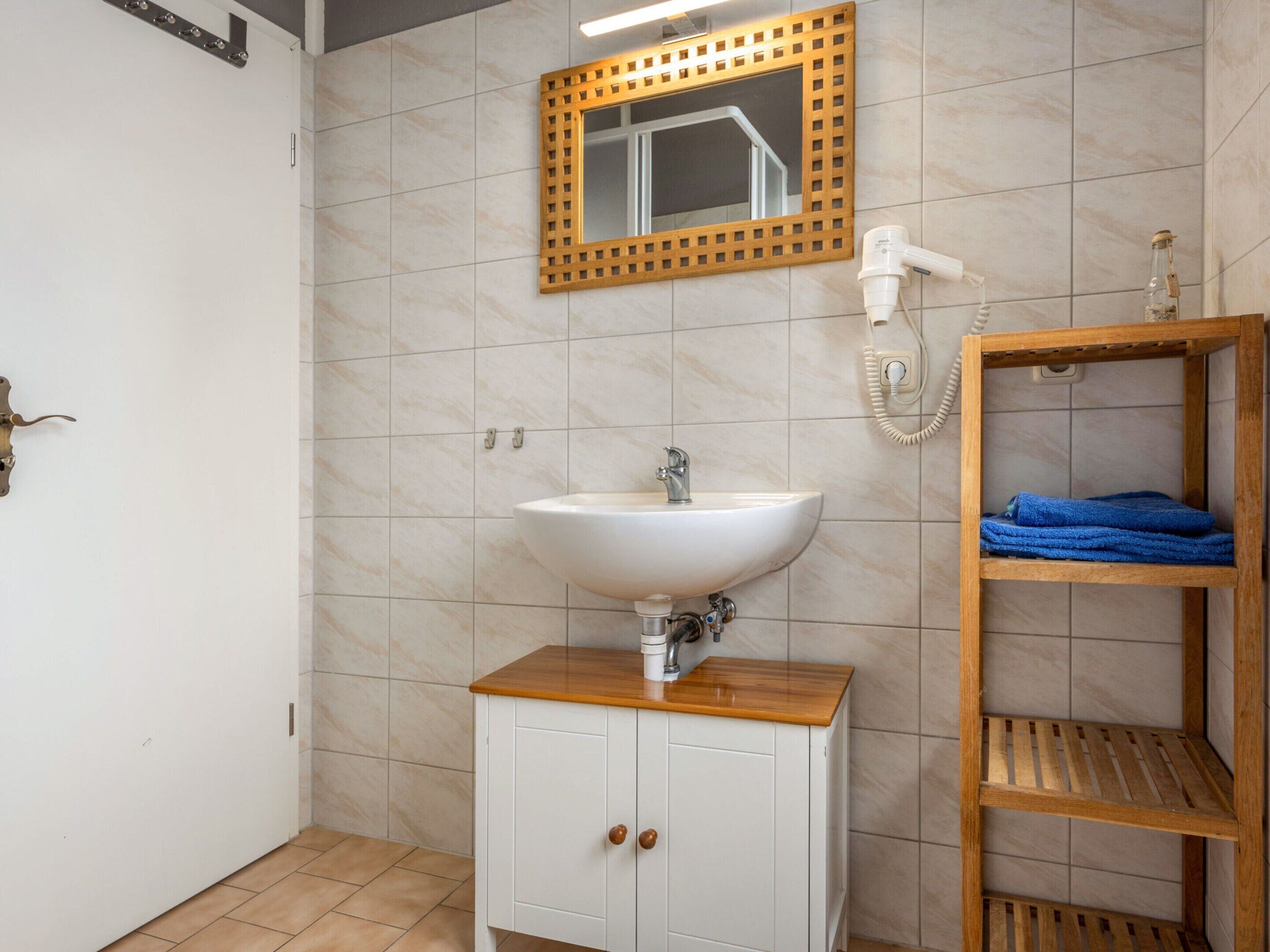 Een badkamer met een witte wastafel, een houten kastje en een plank met handdoeken.