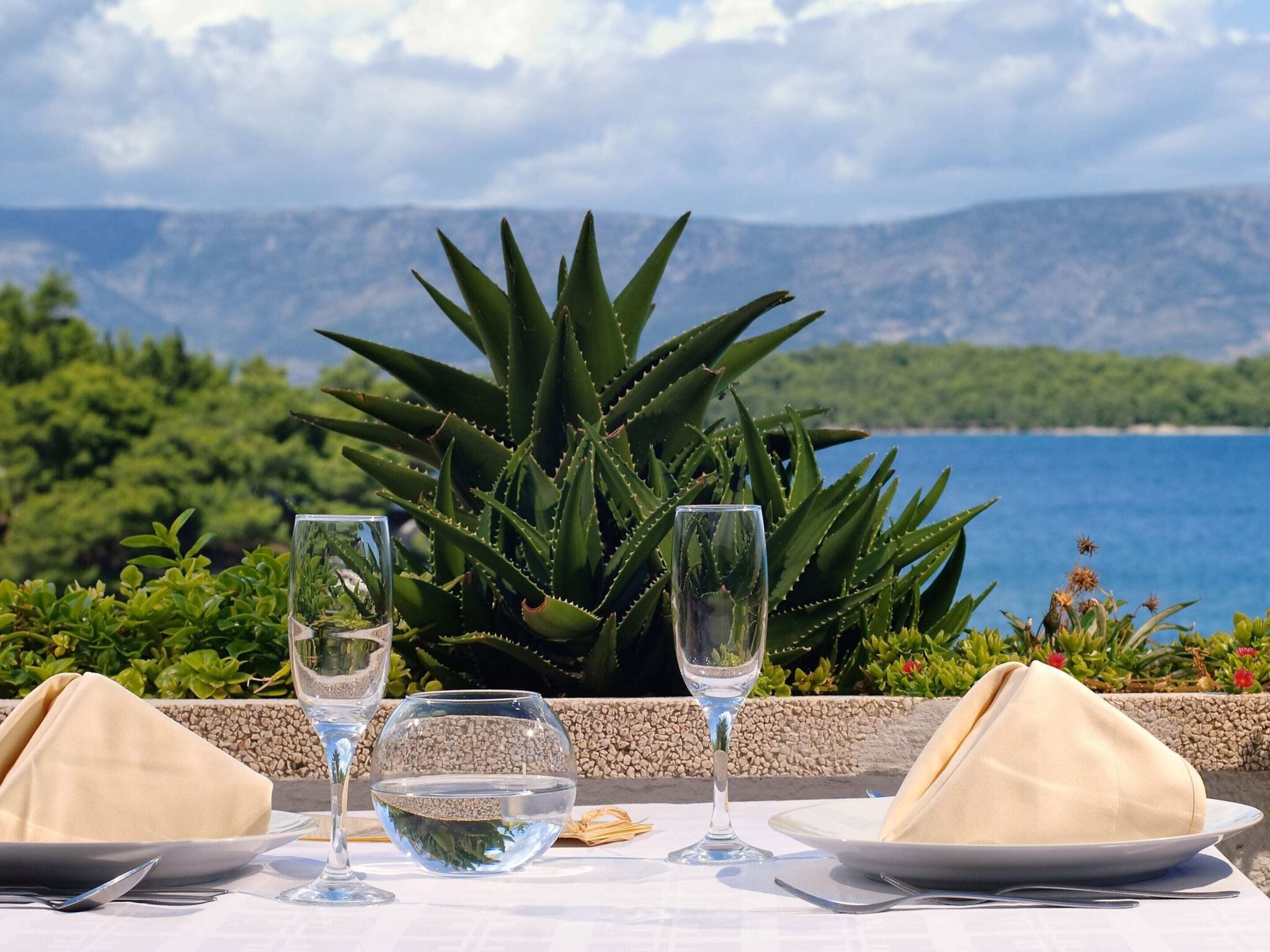 Une table dressée pour deux personnes, offrant une vue dégagée sur un paysage montagneux et une étendue d’eau en arrière-plan.