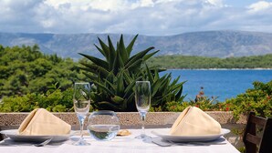 A table set for two with a glass bowl and two wine glasses, overlooking a body of water and greenery. - Beautiful Apartments in Jelsa, With Pool (Jelsa)
