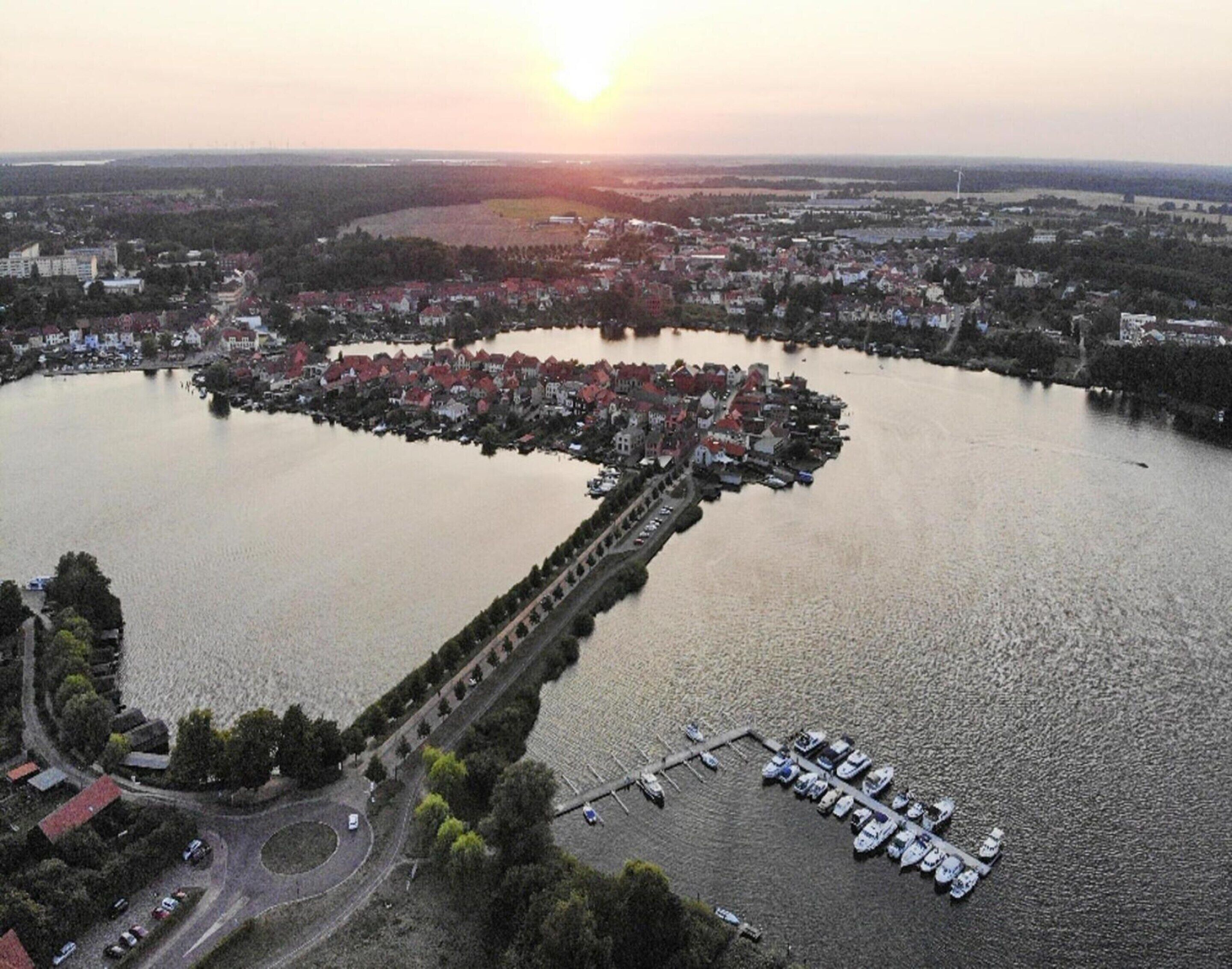 Une vue aérienne d’une zone riveraine, avec un pont reliant deux quartiers d’une ville, un port de plaisance avec des bateaux et des immeubles résidentiels environnants.