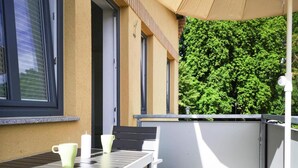 Un balcon avec une table et des chaises, une vue sur un arbre verdoyant et une fenêtre avec des stores.