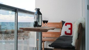 Ein Balkon mit Tisch, auf dem eine Flasche und Gläser stehen, eine Bank mit Kissen und Blick aufs Meer.