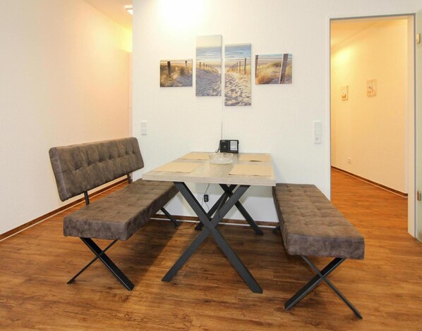 A room with a wooden floor, a table with a radio, two cushioned benches, and four framed pictures on the wall. - Ferienwohnung in Olpenitz Nahe der Ostsee (Kappeln)
