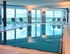 An indoor swimming pool with clear views of the outdoors, surrounded by lounge chairs. - Ferienwohnung in Olpenitz Nahe der Ostsee (Kappeln)