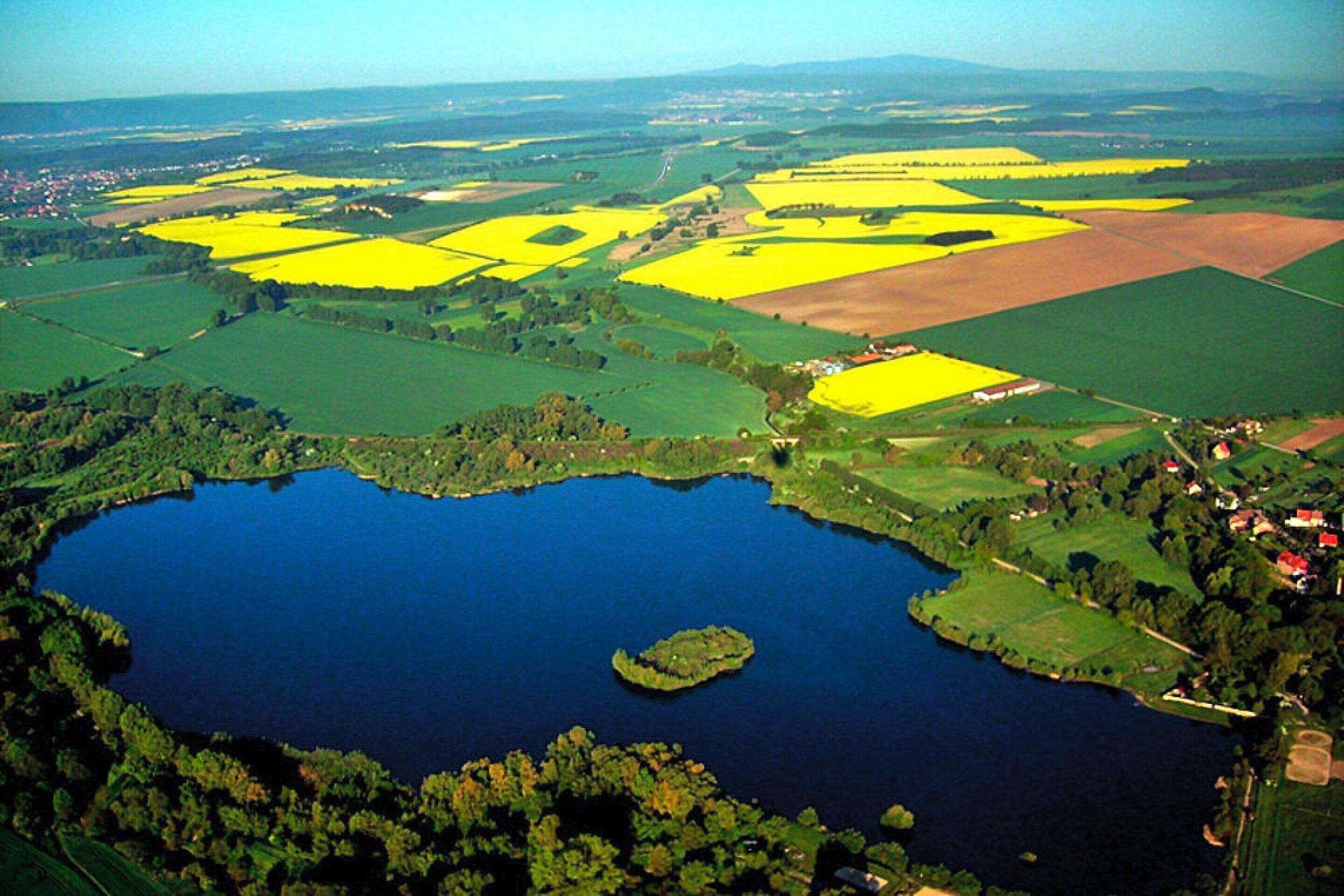 An aerial view of a lake surrounded by fields, with a small island in the center.