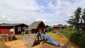 A playground with a slide and climbing wall, surrounded by red buildings and greenery. - Neuer Luxurioser Bungalow, Rauberkuhle, Koserow (Koserow)