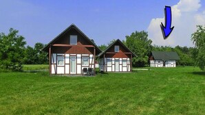 A row of three traditional wooden houses with gabled roofs, set in a grassy field with trees in the background. - Ferienhaus am Partwitzer See, Elsterheide (Elsterheide)