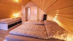 A cozy attic bedroom with a large bed, a small sofa, and a hanging light fixture. - Ferienhaus am Partwitzer See, Elsterheide (Elsterheide)