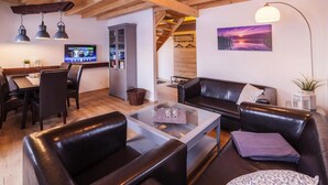 A modern living room with leather sofas, a glass coffee table, and a television in the background. - Ferienhaus am Partwitzer See, Elsterheide (Elsterheide)