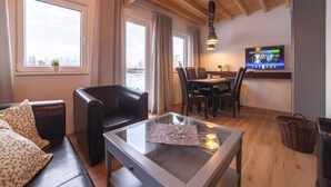 A modern living room with a glass coffee table, leather sofa, and dining area with wooden chairs. - Ferienhaus am Partwitzer See, Elsterheide (Elsterheide)