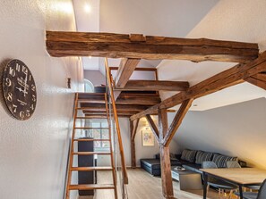 Una camera in stile loft con travi a vista in legno, un letto soppalco, una scala e una sveglia appesa al muro.