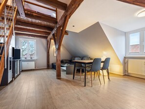 A loft-style room with a dining area, wooden beams, a window, and a radiator.
