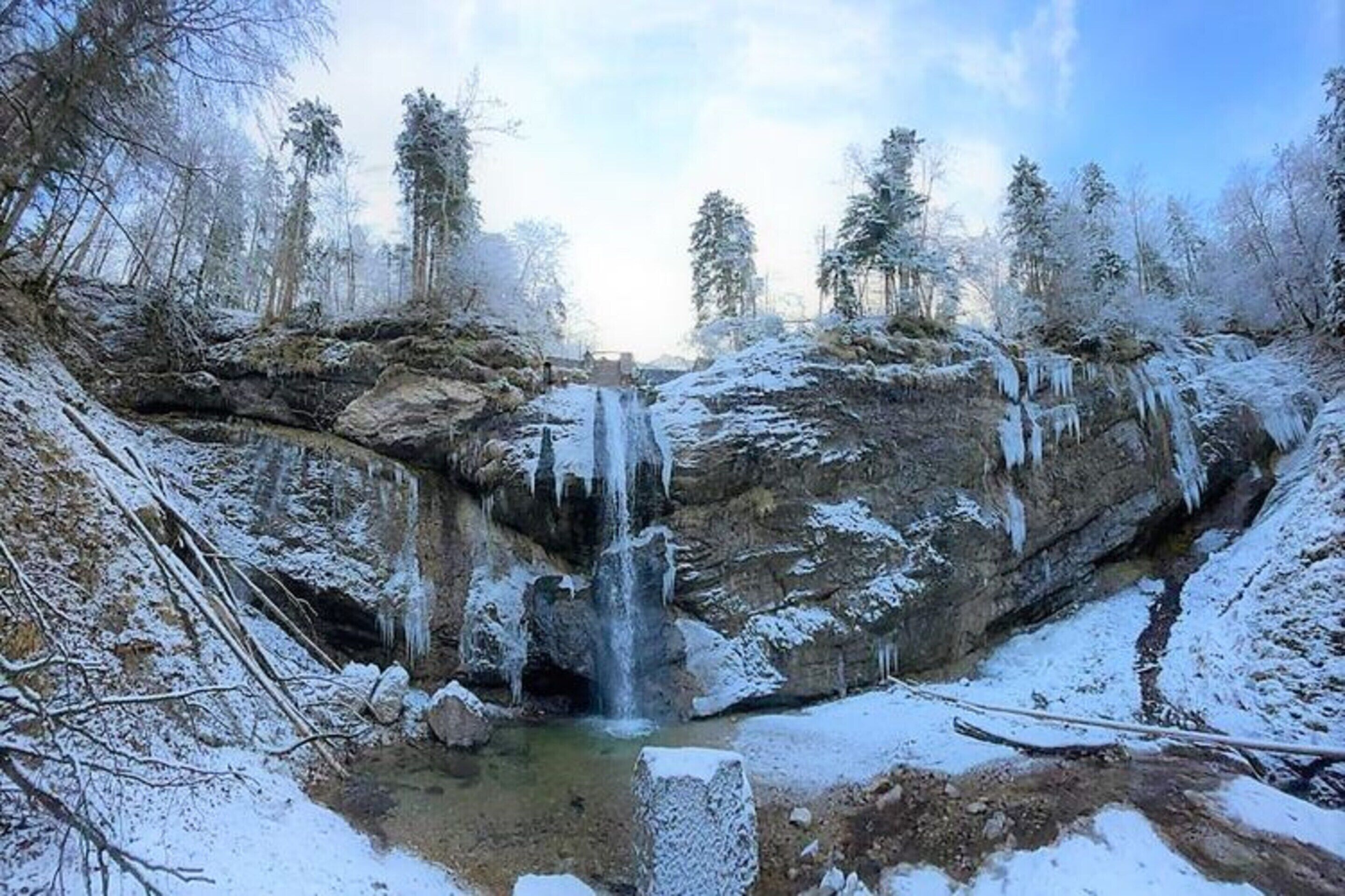 Een winters landschap met een waterval, sneeuwbedekte bomen en een heldere lucht.