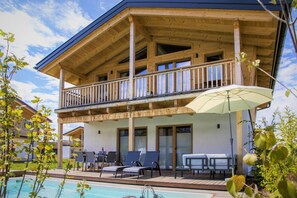 A wooden chalet with a balcony, outdoor seating, and a pool.