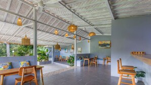 A spacious indoor area with wooden furniture, hanging light fixtures, and a view of greenery outside. - La Rise Penida Cottage (Penida Island)