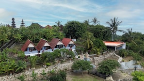 A traditional Balinese village with thatched-roof houses, a stone staircase, and lush greenery.