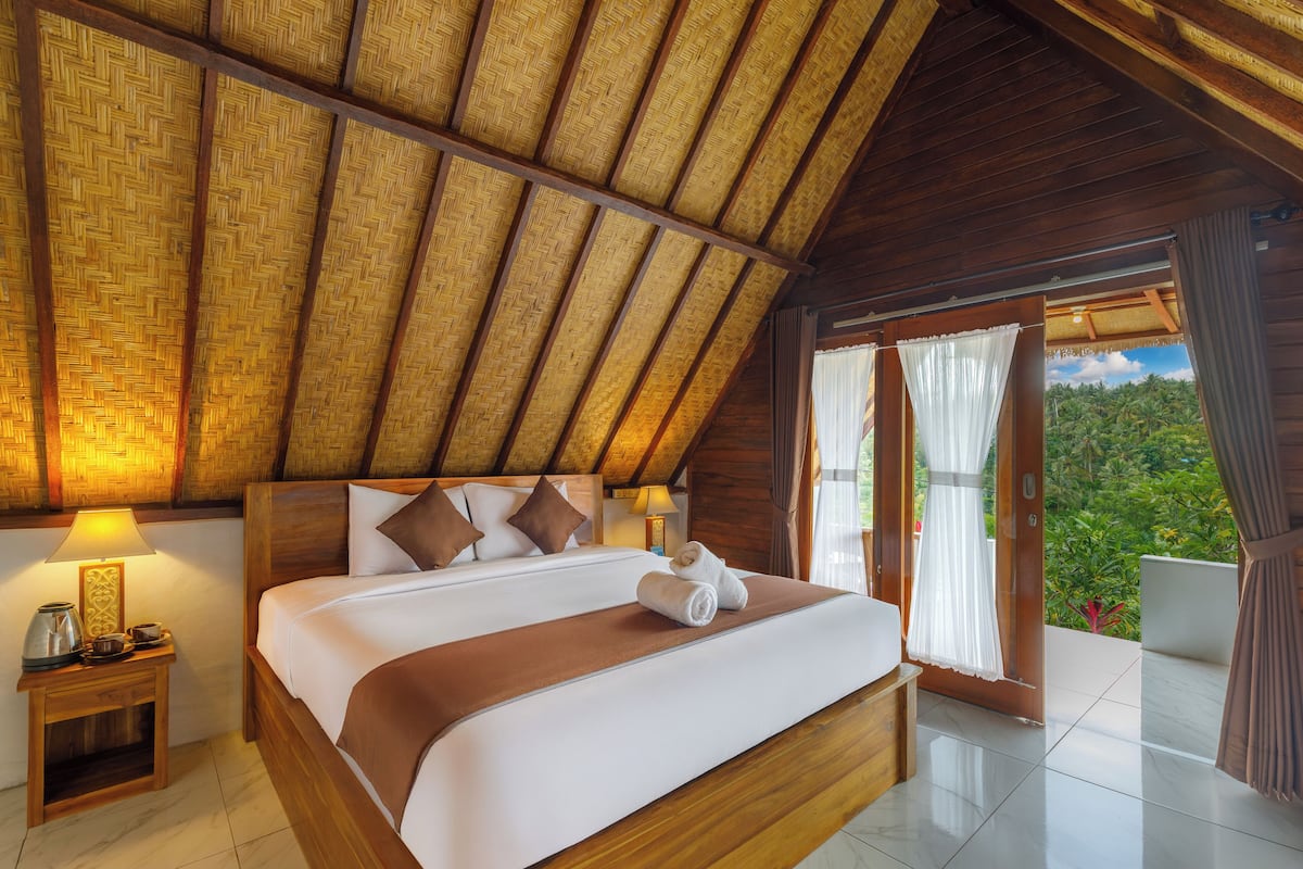 A spacious room with a large bed, wooden headboard, and a thatched ceiling.