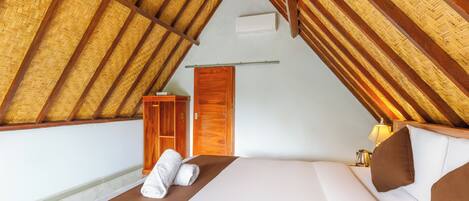 A bedroom with a sloped ceiling, a wooden wardrobe, a bed with white and brown bedding, and a nightstand with a lamp.