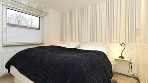 Une chambre à coucher avec un lit, une fenêtre avec des stores, une lampe de chevet et un mur à rayures.