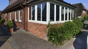 Une maison à deux étages, avec une façade en briques et une véranda aux montants blancs.